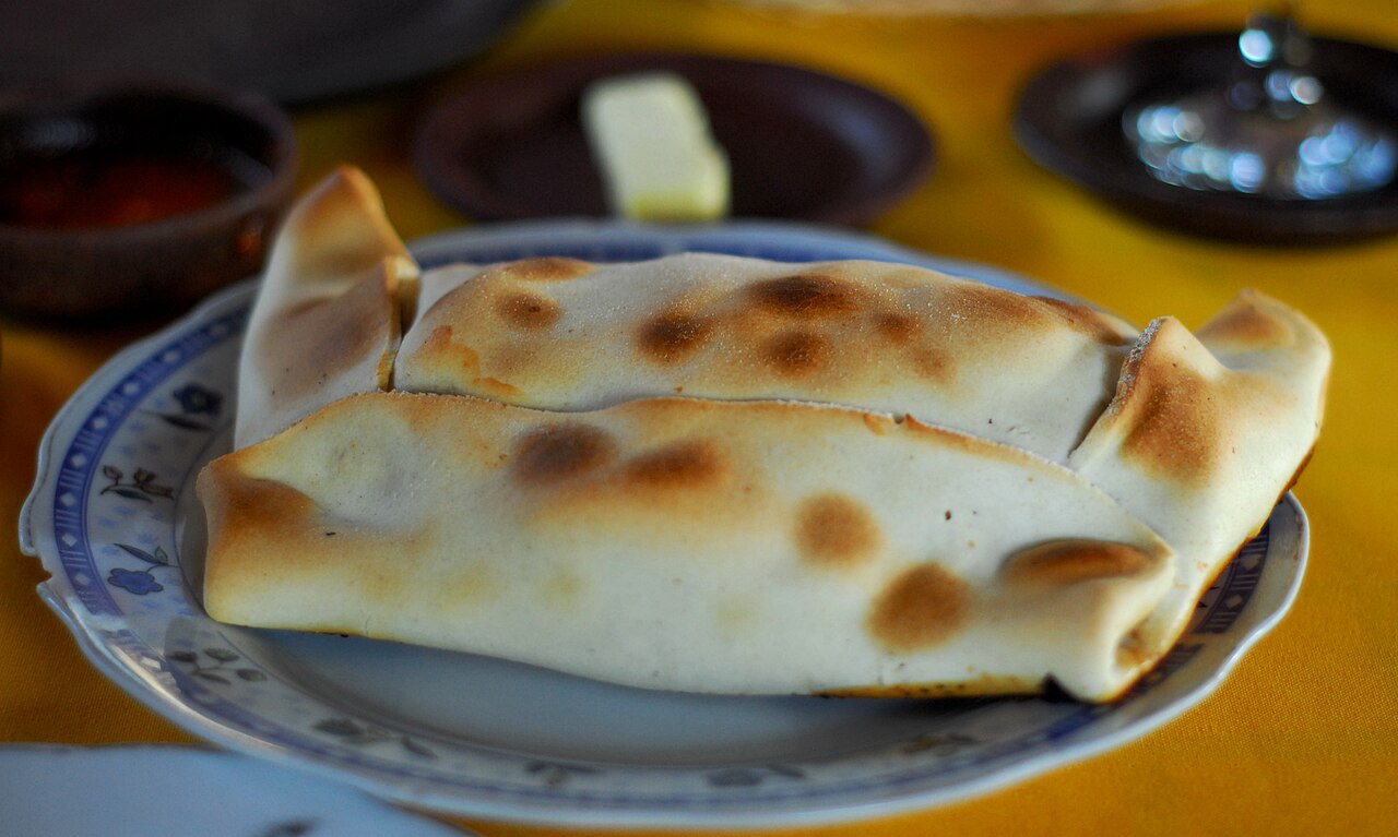 Photoreal photograph of the finished dish Empanada de pino, the actual plate from Chile, handmade ceramic, natural window light, shallow depth of field, no text, no logo, no people, Natural window light, ivory linen, handmade ceramic, shallow depth of field, no text, no logo, no watermark, fine-dining magazine photograph. Empanada de pino