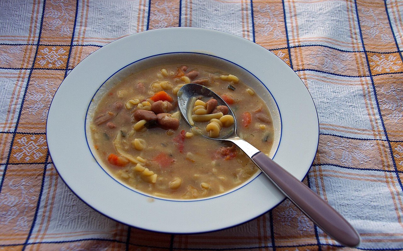 Photoreal photograph of the finished dish Pasta e fagioli, the actual plate from Italy, handmade ceramic, natural window light, shallow depth of field, no text, no logo, no people, Natural window light, ivory linen, handmade ceramic, shallow depth of field, no text, no logo, no watermark, fine-dining magazine photograph. Pasta e fagioli