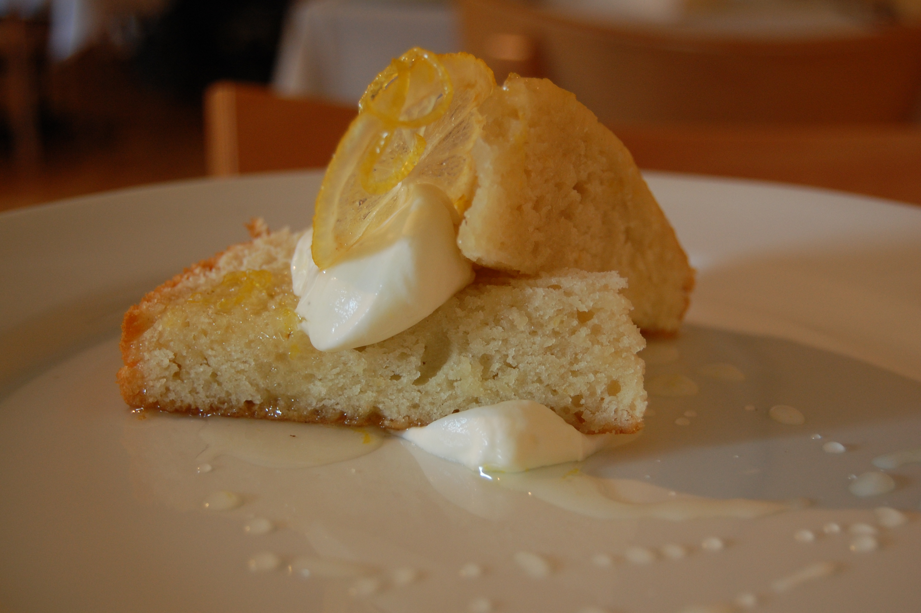 A slice of lemon olive oil cake, yellow crumb, glaze barely there, Natural window light, ivory linen, handmade ceramic, shallow depth of field, no text, no logo, no watermark, fine-dining magazine photograph. Lemon Olive Oil Cake