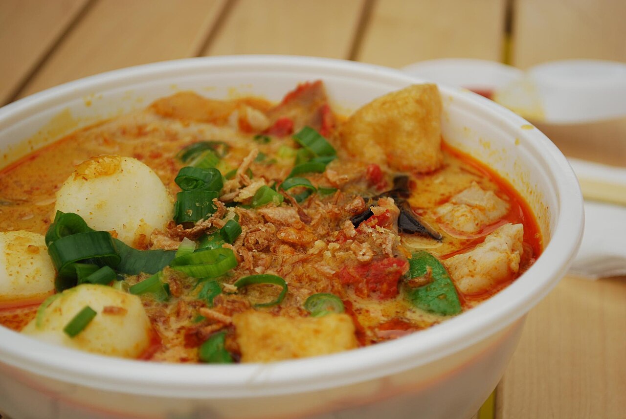 Photoreal photograph of the finished dish Curry laksa (laksa), the actual plate from Malaysia, handmade ceramic, natural window light, shallow depth of field, no text, no logo, no people, Natural window light, ivory linen, handmade ceramic, shallow depth of field, no text, no logo, no watermark, fine-dining magazine photograph. Curry laksa