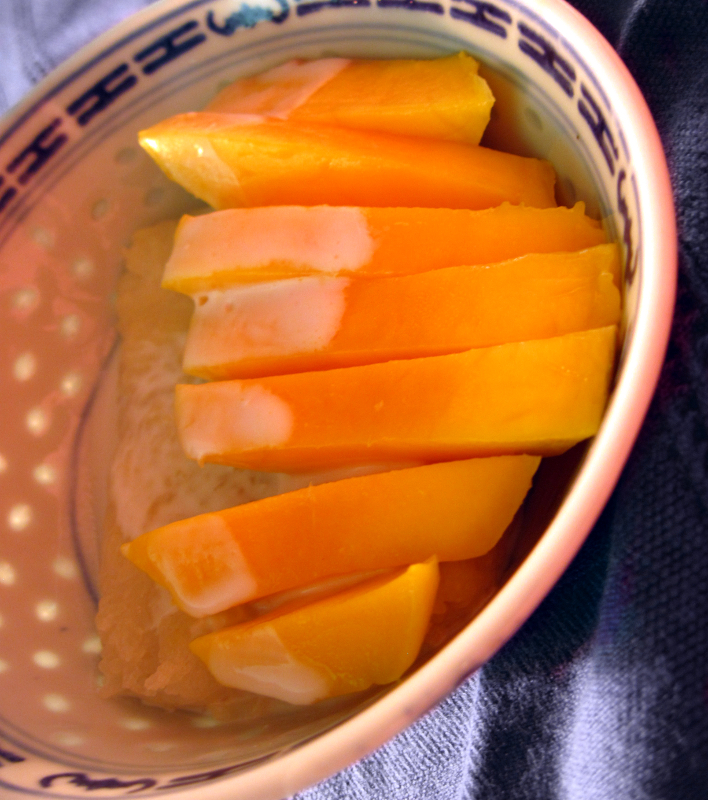 Sliced ripe mango beside glossy coconut sticky rice, sesame, a gold spoon, Natural window light, ivory linen, handmade ceramic, shallow depth of field, no text, no logo, no watermark, fine-dining magazine photograph. Mango Coconut Sticky Rice