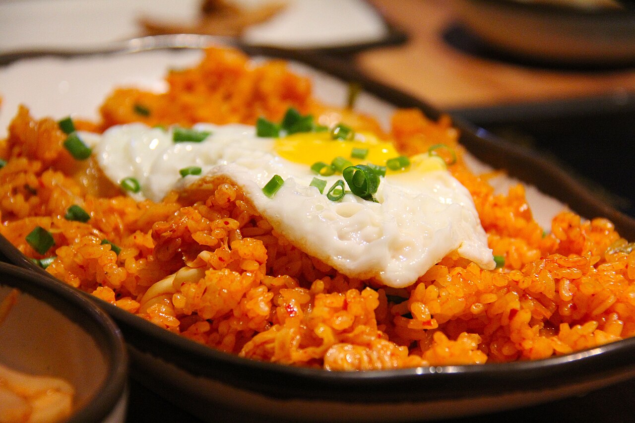 Photoreal photograph of the finished dish Kimchi fried rice (김치볶음밥), the actual plate from South Korea, handmade ceramic, natural window light, shallow depth of field, no text, no logo, no people, Natural window light, ivory linen, handmade ceramic, shallow depth of field, no text, no logo, no watermark, fine-dining magazine photograph. Kimchi fried rice
